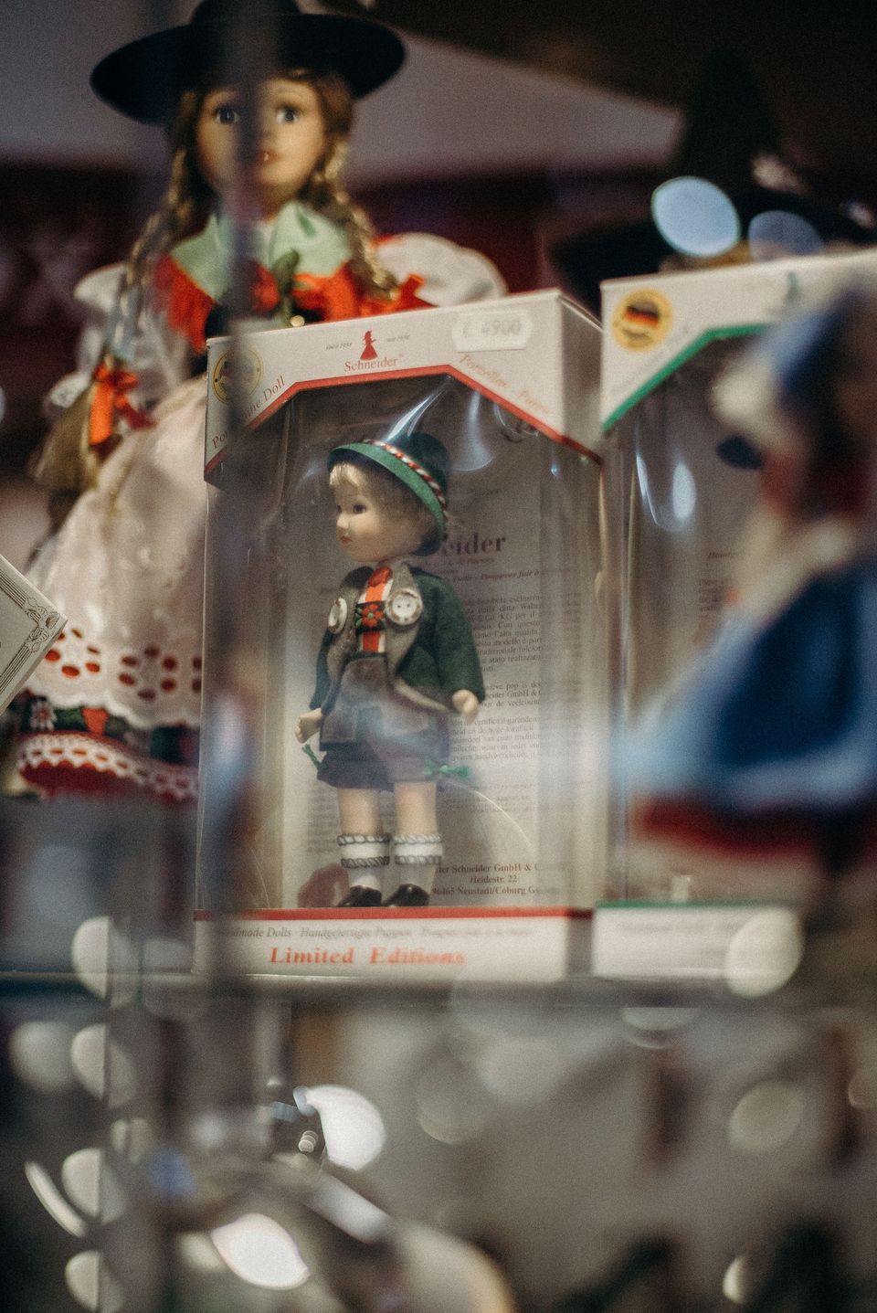 Doll in a green felt jacket, embroidered braces and green hat displayed inside a clear window box