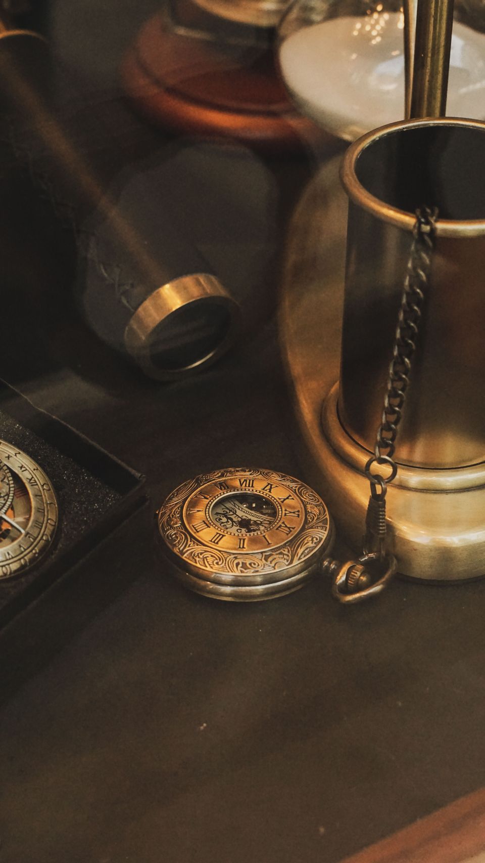 Close-up of an engraved brass pocket watch with Roman numerals beside a brass cylinder and chain