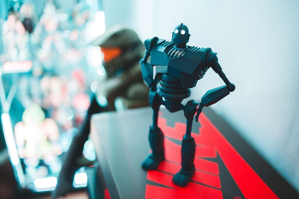 Dark riveted robot figure with glowing white eyes standing with one hand on its hip